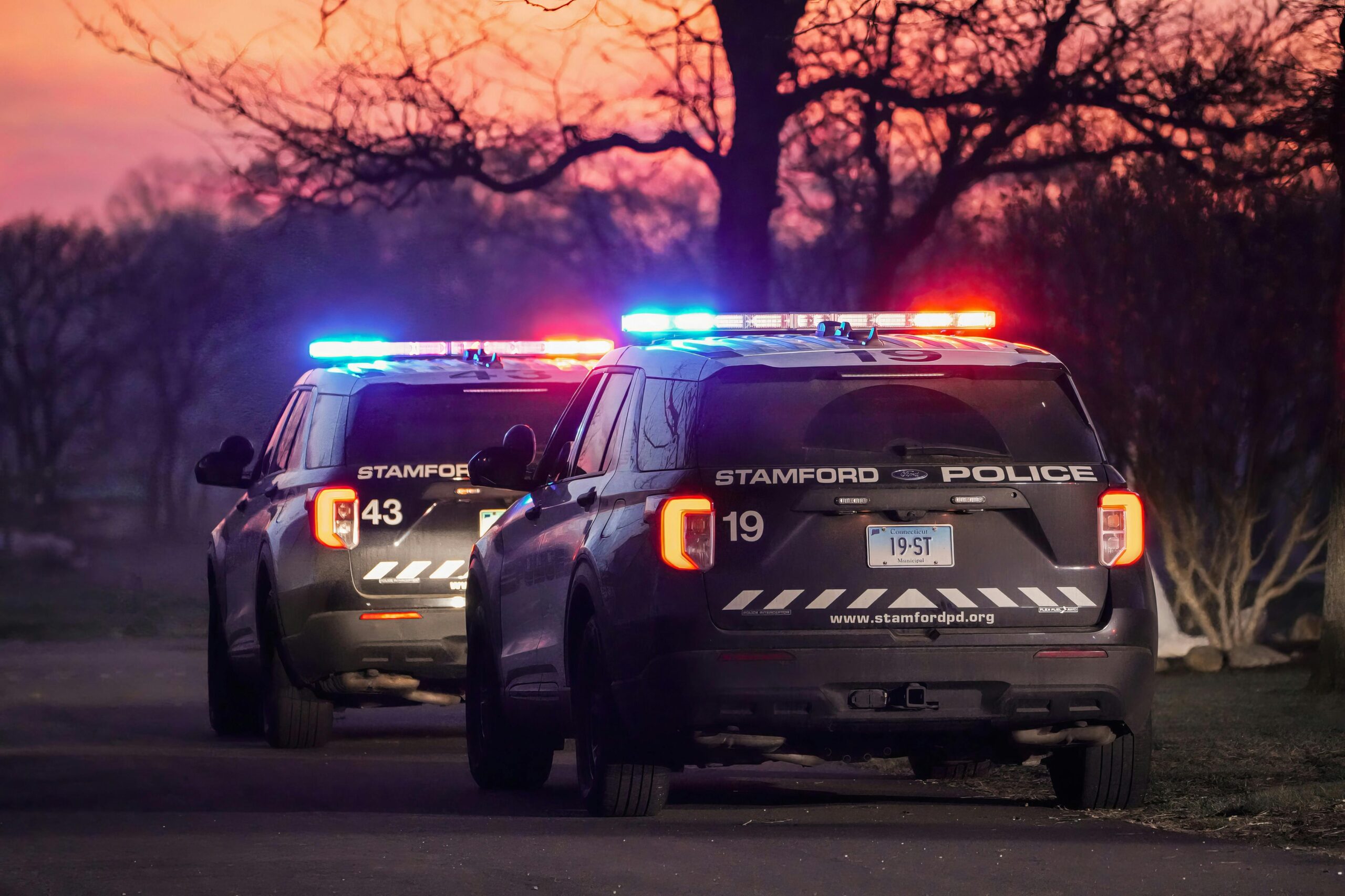 Stamford police cars with flashing lights during a vibrant sunset setting.