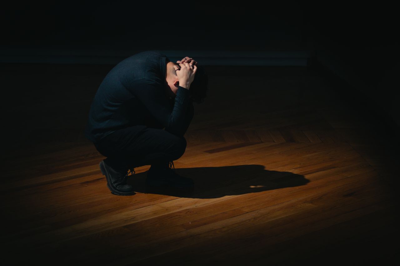 A person crouching alone in darkness, conveying solitude and emotion.